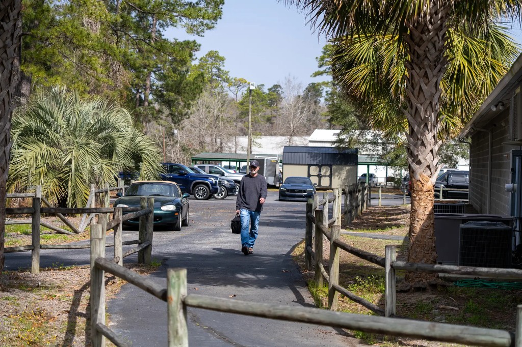 Guest walking toward Lowcountry Guns along the fenced entrance path, parking and trees in the background
