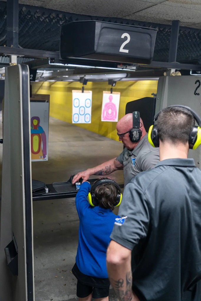 Instructor assisting a young shooter at the range, lane 2, with eye and ear protection